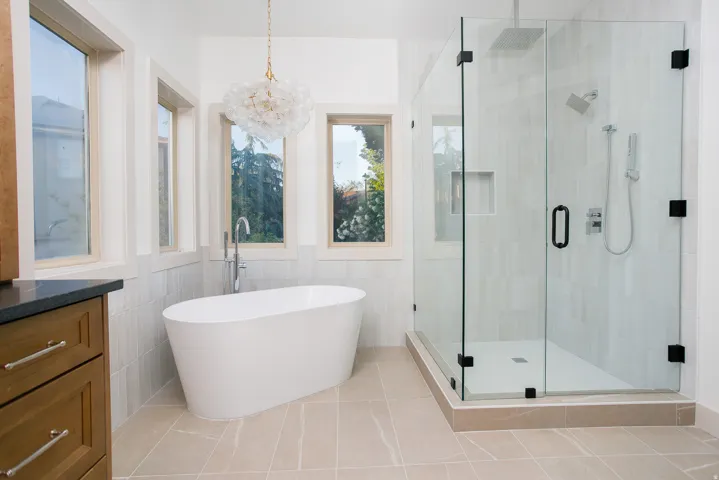 Contemporary bathroom featuring a freestanding soaking tub with a floor-mounted faucet, a glass-enclosed shower with black hardware, and light-toned tile flooring