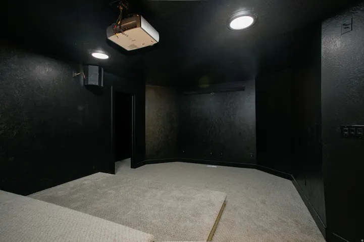 Dedicated entertainment space featuring a ceiling-mounted projector, recessed lighting, and wall-mounted speakers