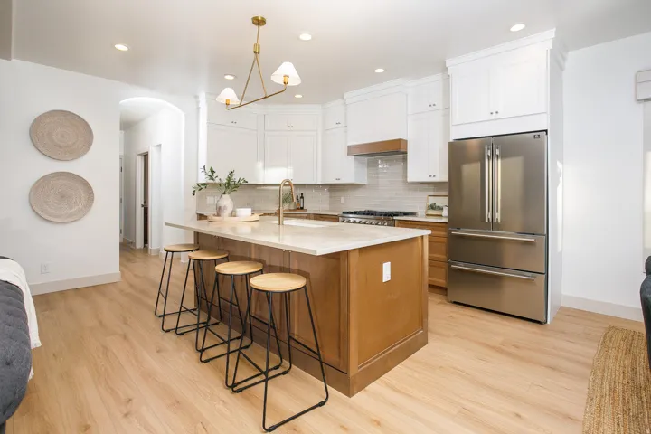 Bright kitchen featuring a large central island with seating, light-toned wood-finish flooring, white upper cabinetry, and stainless steel appliances