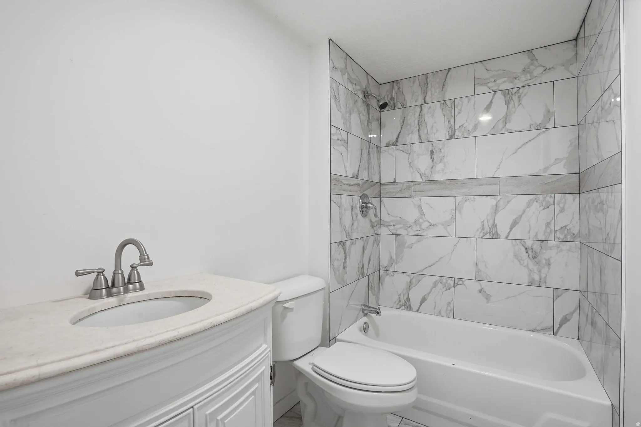 Bathroom featuring a white vanity with an oval undermount sink and light-toned countertop, brushed nickel faucet, white toilet, and a white tub with a tiled surround
