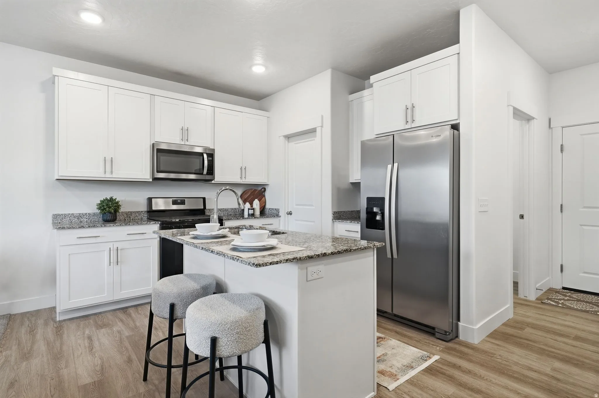Contemporary open-concept kitchen featuring white shaker cabinetry, Gas stove, stainless steel appliances, a center island, granite countertops