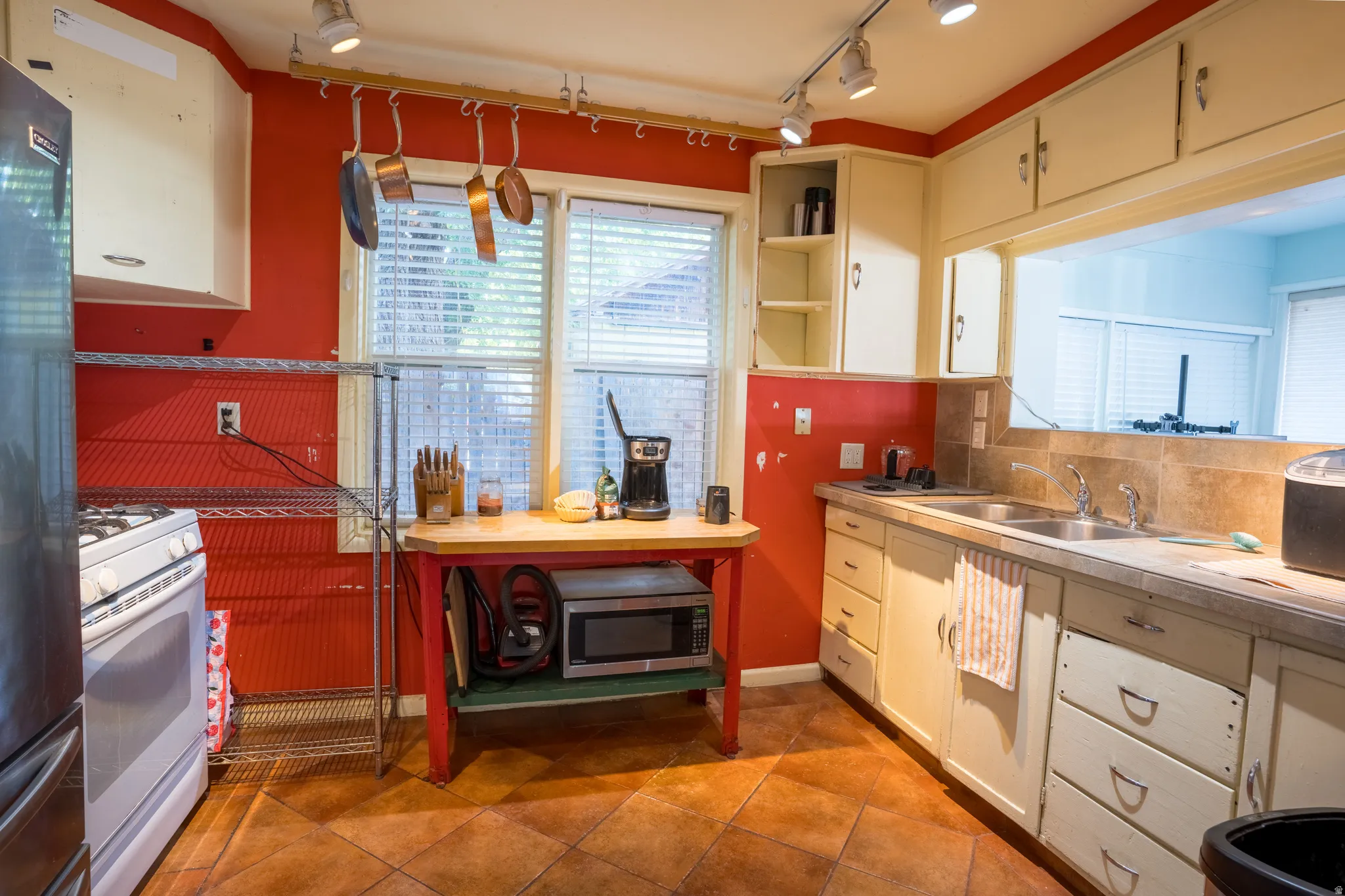 Kitchen with decorative backsplash, white range with gas cooktop, freestanding refrigerator, rail lighting, and light countertops
