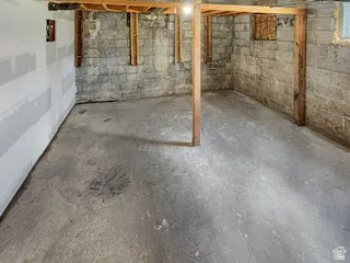 Unfinished basement offering concrete block walls, exposed wooden structural beams, and a concrete floor