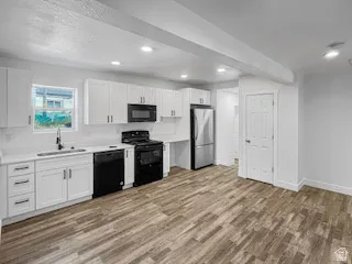 Bright kitchen featuring white cabinetry, light countertops, wood-finish flooring, a stainless steel refrigerator, and a black range