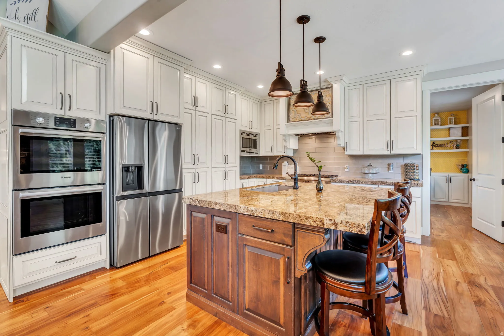 Gourmet kitchen featuring a center island with pendant lighting, stainless steel appliances, extensive white cabinetry, and wood-finish flooring