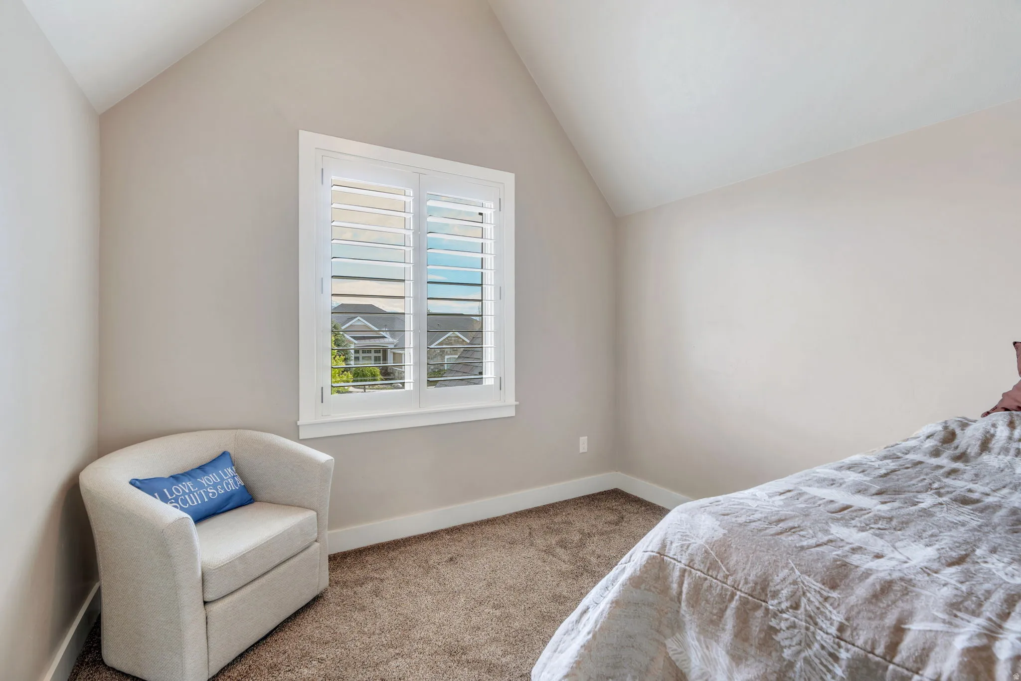 Vaulted ceiling room featuring a window with white plantation shutters, neutral-toned walls, white trim, and plush carpet flooring