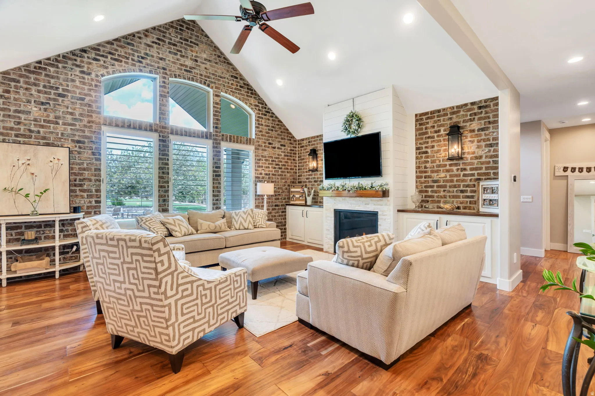 Vaulted great room featuring rich wood-finish flooring, exposed brick accents, and a ceiling fan