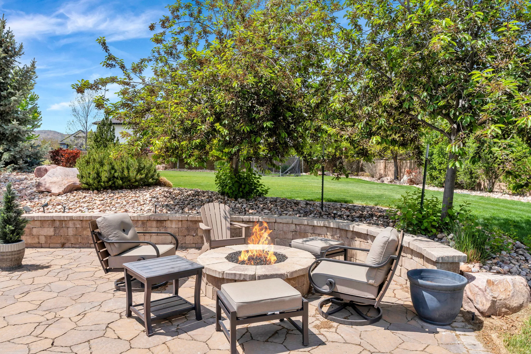 Stone paver patio featuring a built-in fire pit, surrounded by a low retaining wall with stone cap