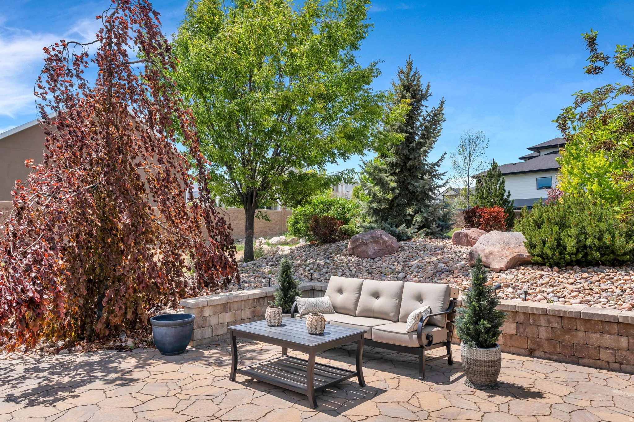 Flagstone patio with a stone retaining wall, xeriscaped landscaping, and mature trees