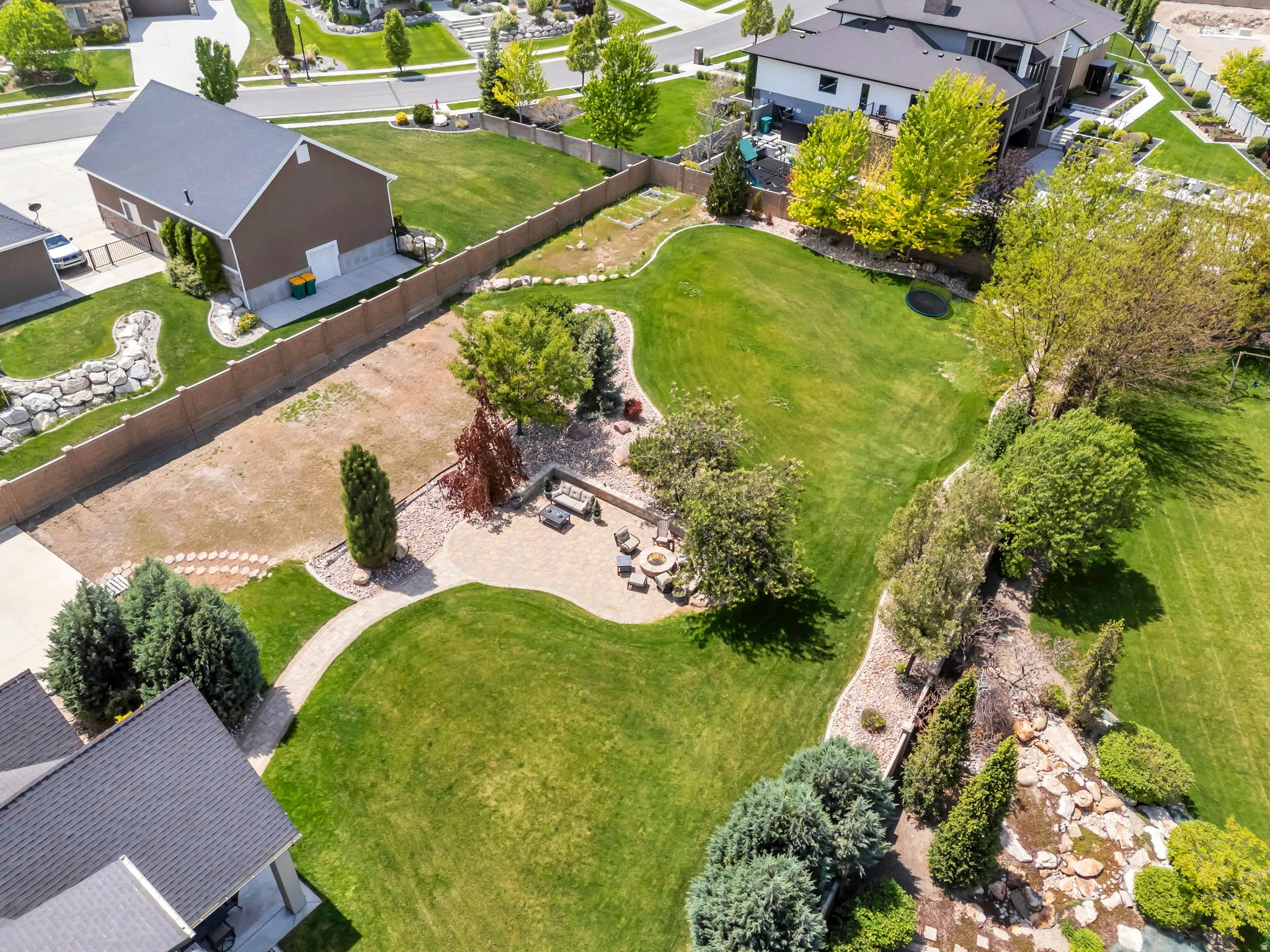Spacious backyard featuring extensive manicured lawns, a curved stone patio, a meandering stone pathway, and mature landscaping