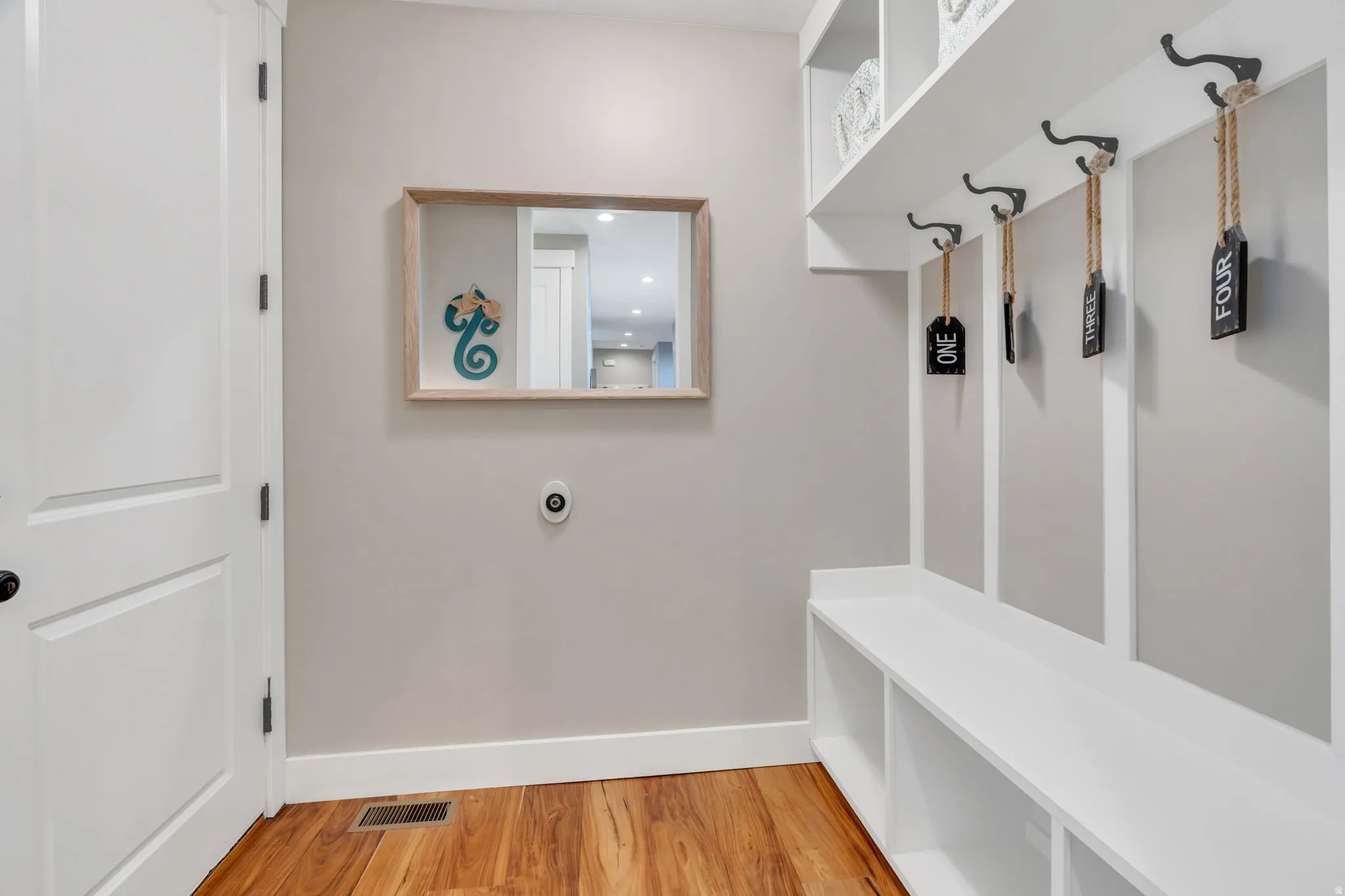 Entryway featuring wood-finish flooring, white built-in bench with integrated storage cubbies, white wall paneling, and black wall-mounted hooks