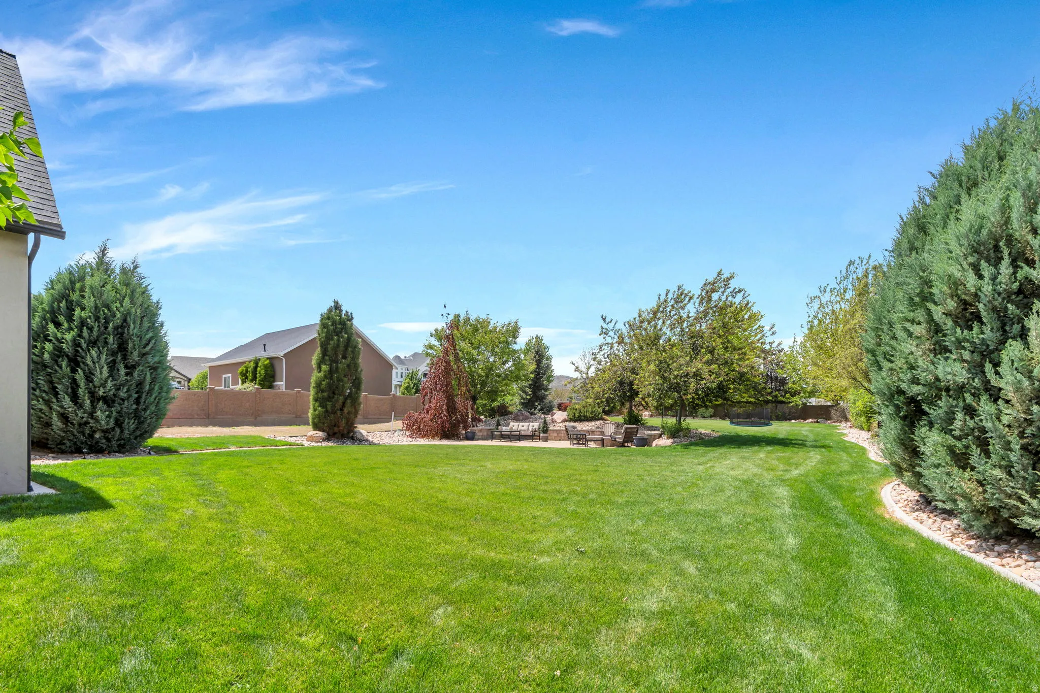 Expansive backyard featuring a lush lawn, mature evergreen landscaping, and a dedicated patio area