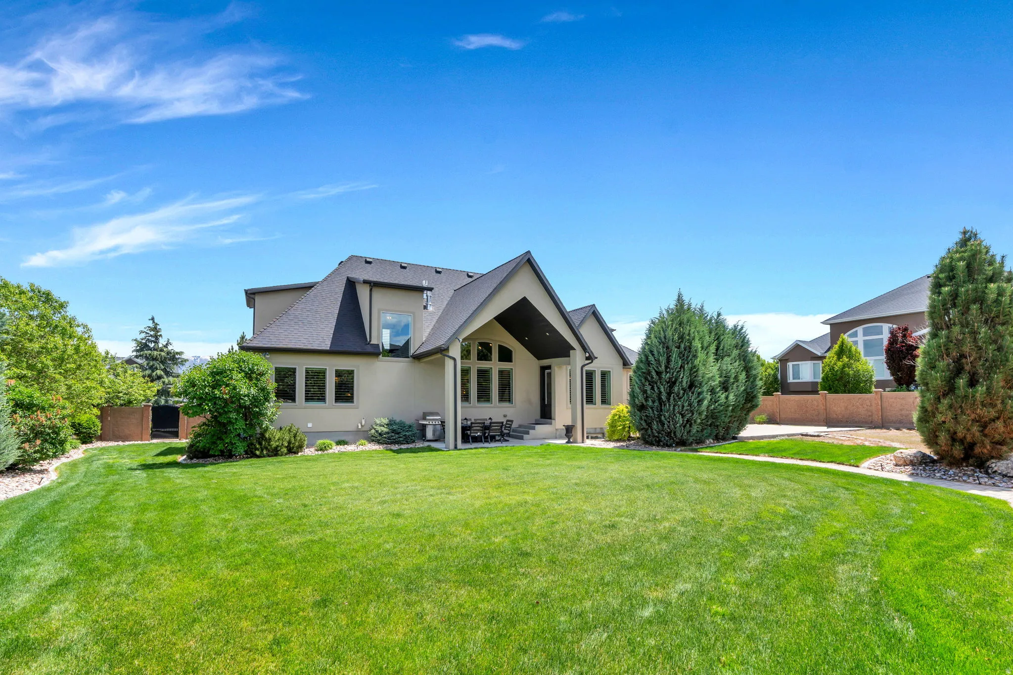Expansive rear yard featuring a manicured lawn, established landscaping, and a covered patio