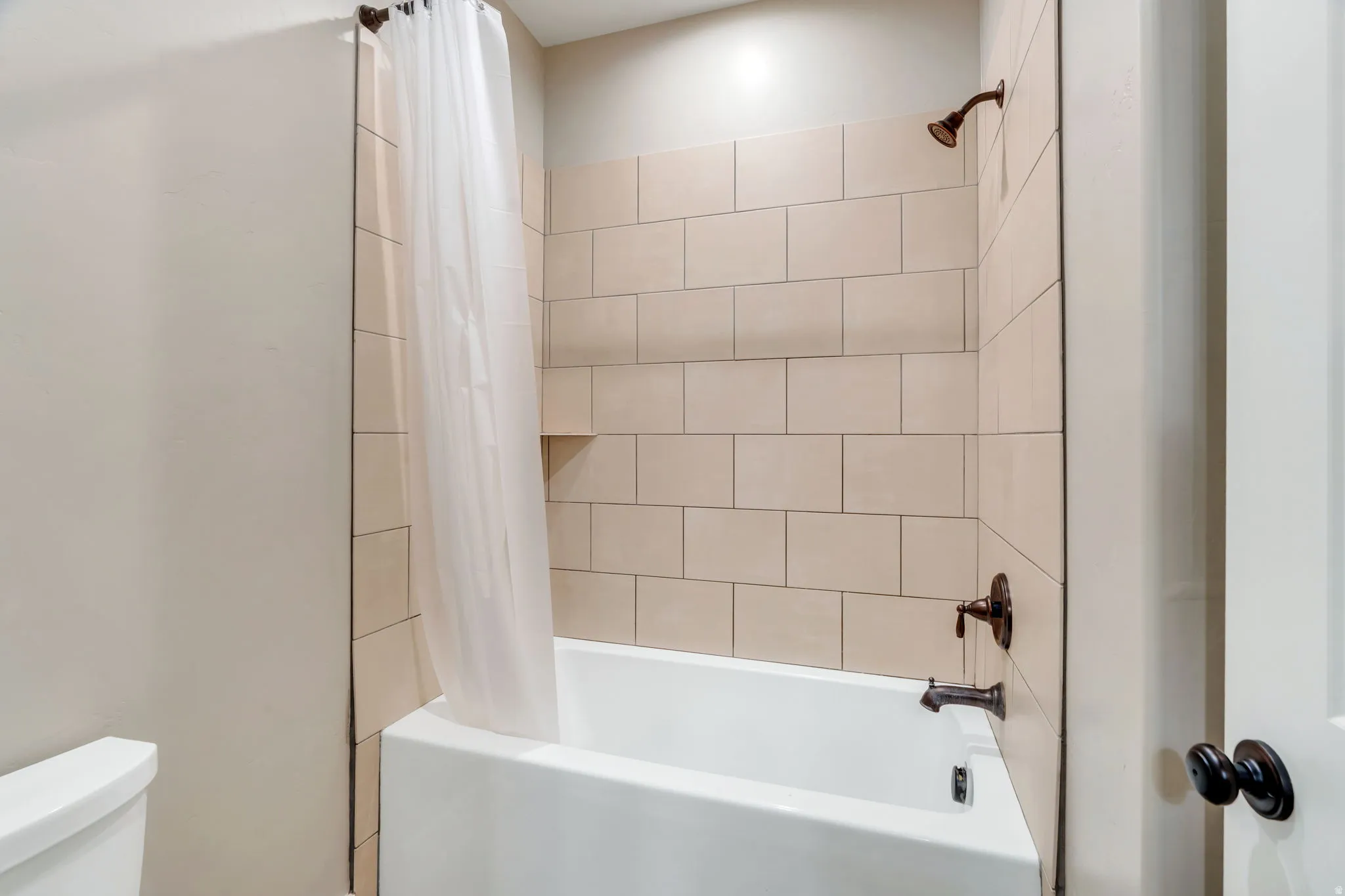 Bathtub with subway tile surround, integrated shower niche, and dark bronze fixtures