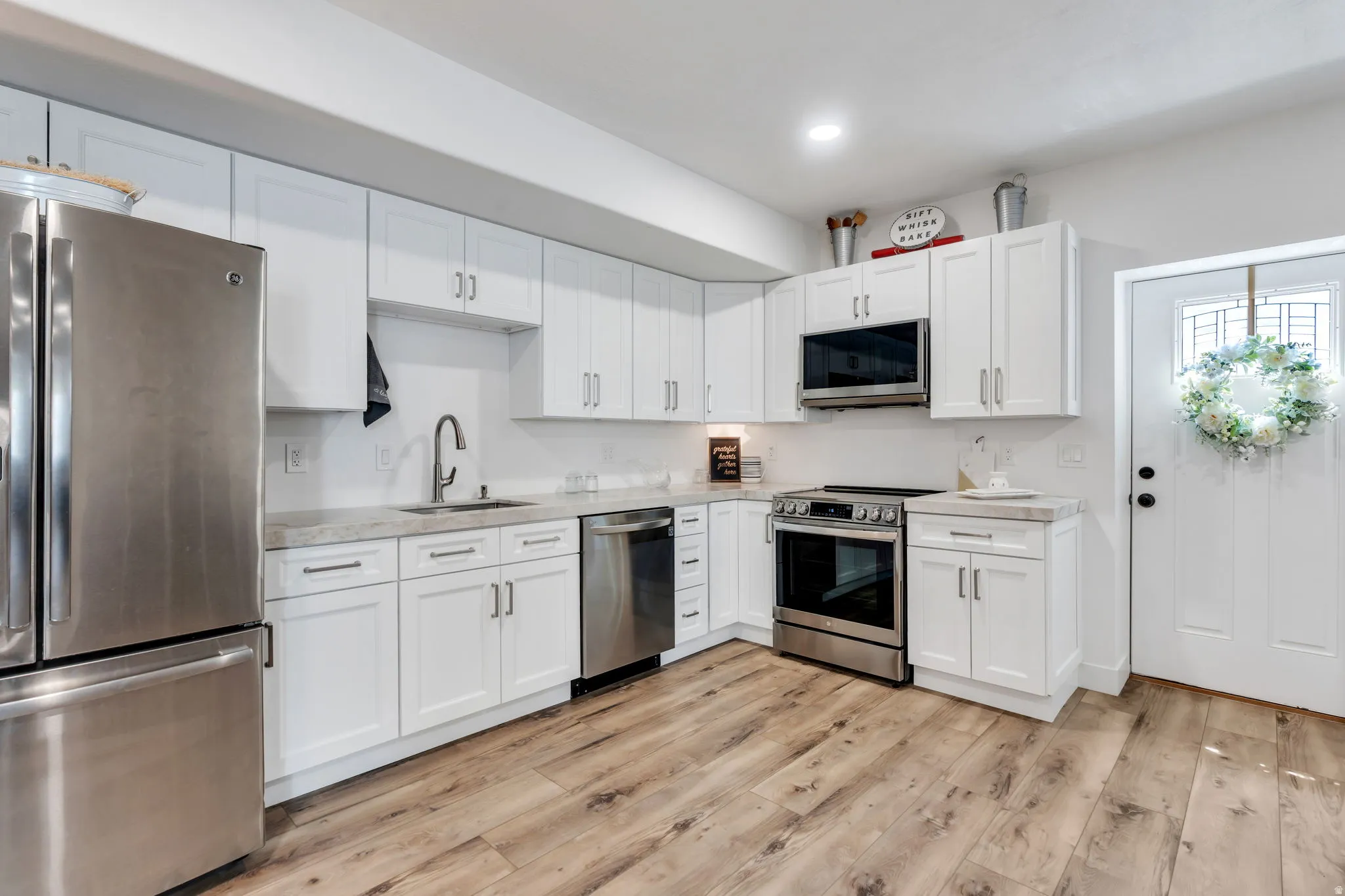 Kitchen featuring white cabinetry, stainless steel appliances, wood-finish flooring, undermount sink, and light-toned countertops