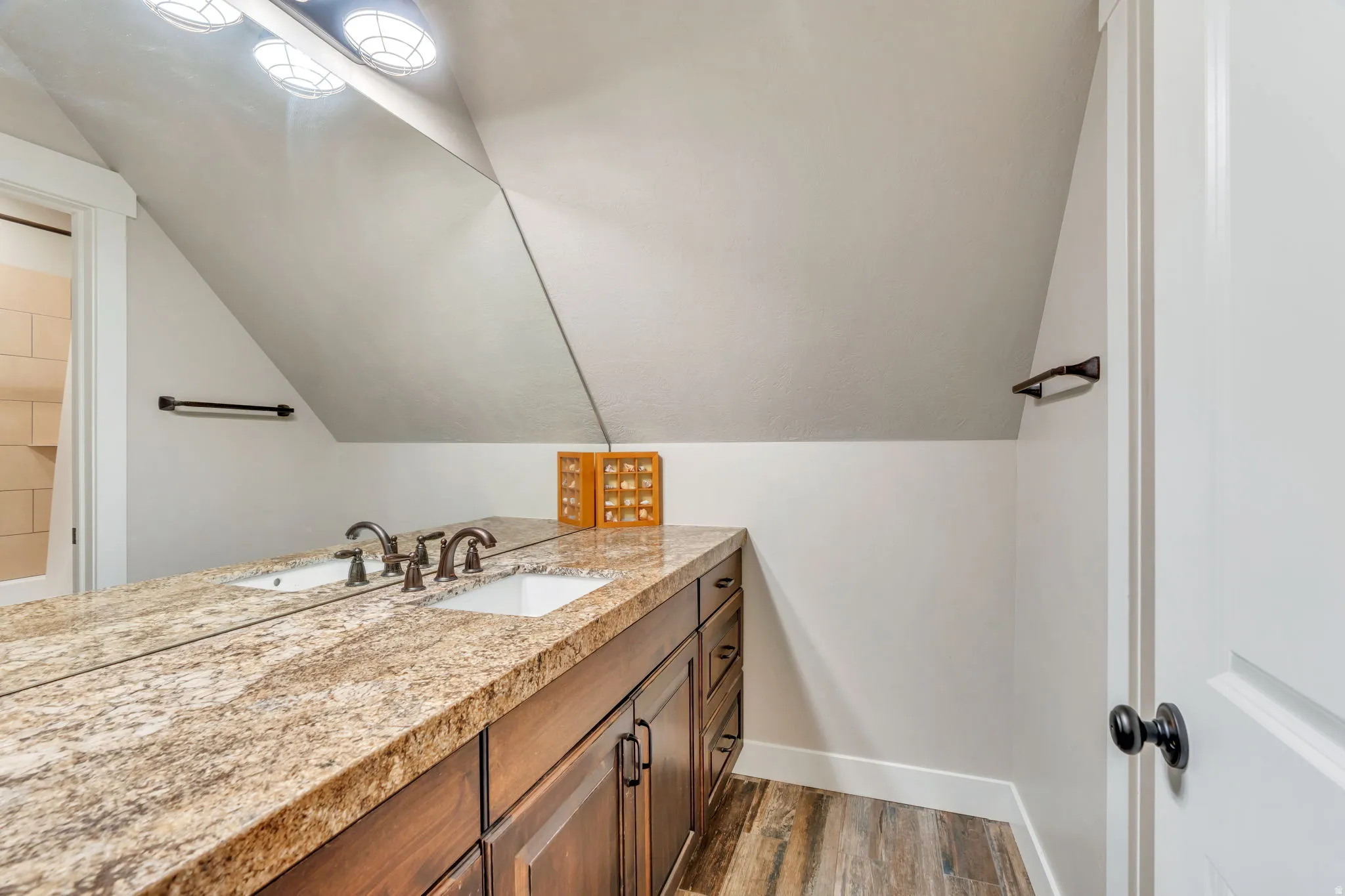 Dual undermount sinks set into a spacious stone countertop, complementing rich wood-finish cabinetry with dark hardware