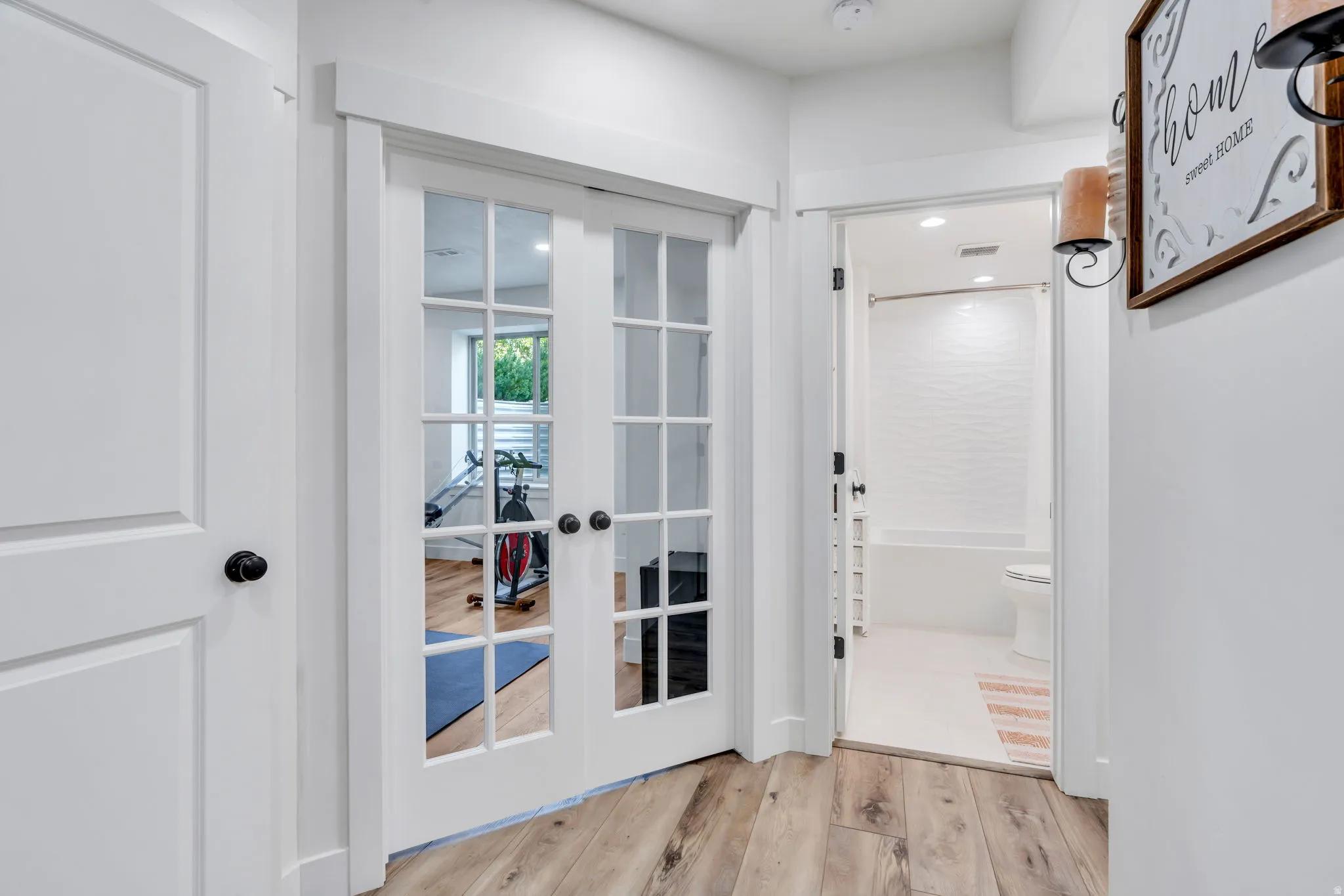 Hardwood-finish flooring throughout, featuring a white paneled door with black hardware, and French doors with black hardware