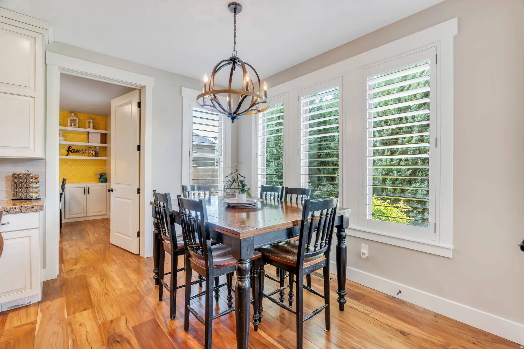 Dining area featuring a contemporary chandelier, wood-finish flooring, and multiple windows with white plantation shutters