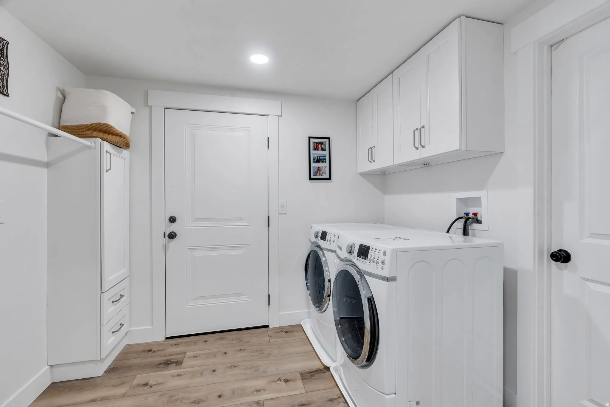 Dedicated laundry area featuring wood-finish flooring, white shaker-style cabinetry, a built-in hanging rod, and recessed lighting