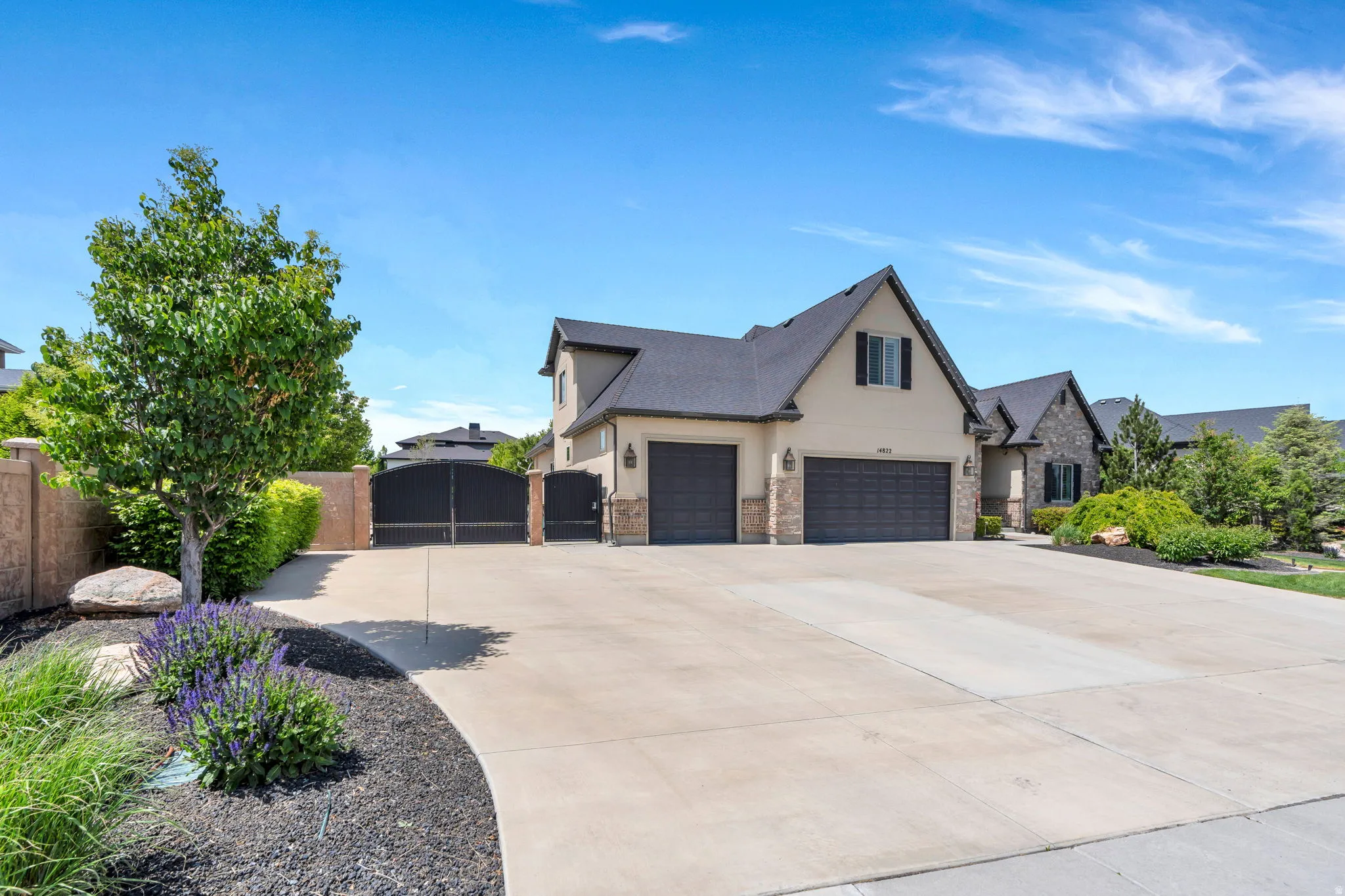 Expansive concrete driveway leading to a residence featuring a stucco and stone exterior