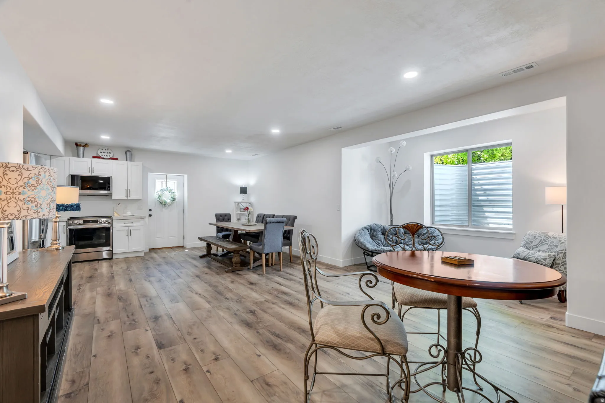 Open-concept living space featuring wood-finish flooring, recessed lighting, and a white kitchen with stainless steel appliances