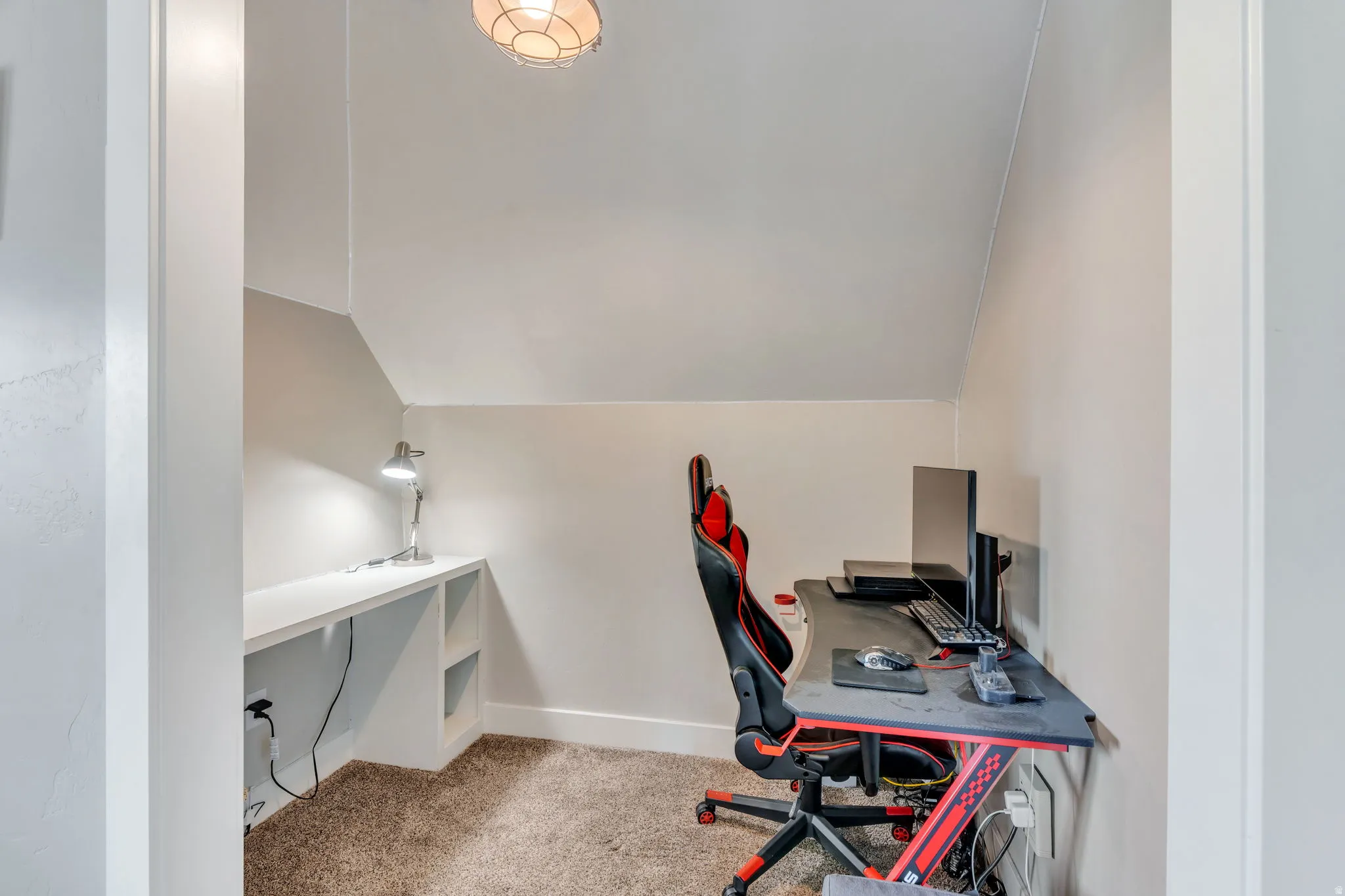 Built-in desk with integrated shelving, sloped ceiling, recessed lighting, and carpet flooring