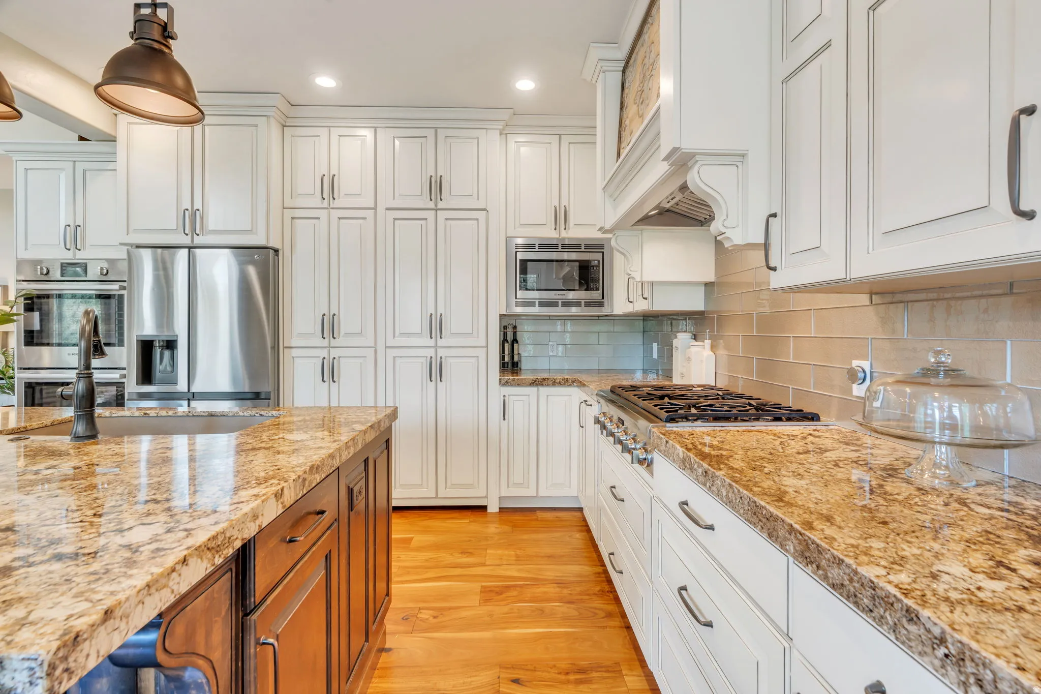Kitchen featuring a large central island with a built-in sink and dark cabinetry, perimeter white cabinetry, stainless steel appliances, a gas range, and wood-finish flooring