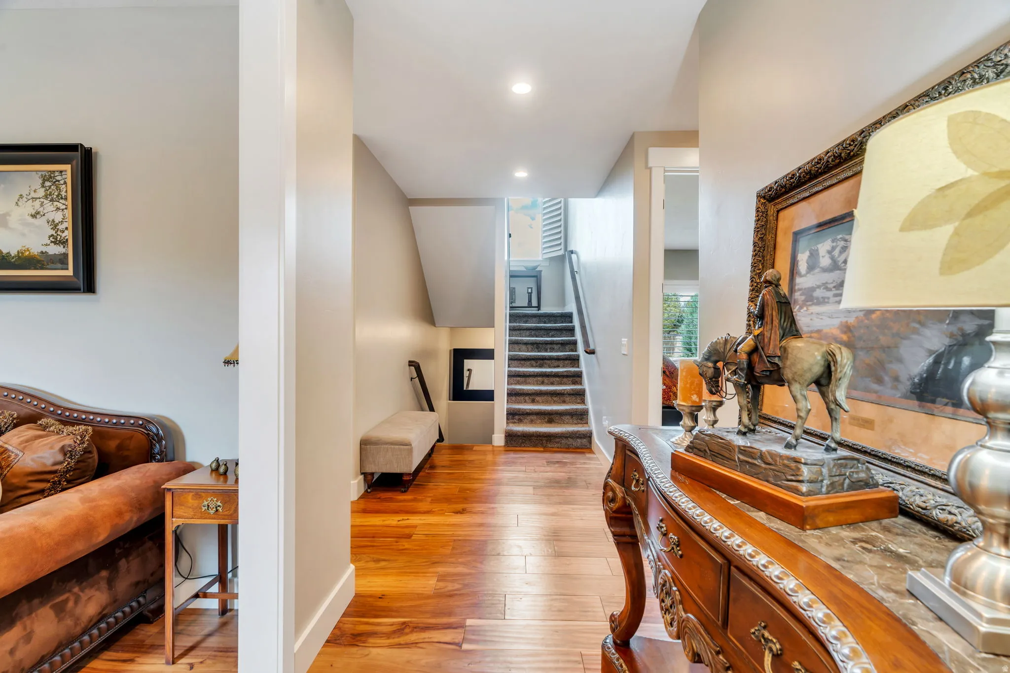 Hardwood flooring extending through the entry, recessed ceiling lighting, a carpeted staircase with white risers, and a built-in bench under the staircase