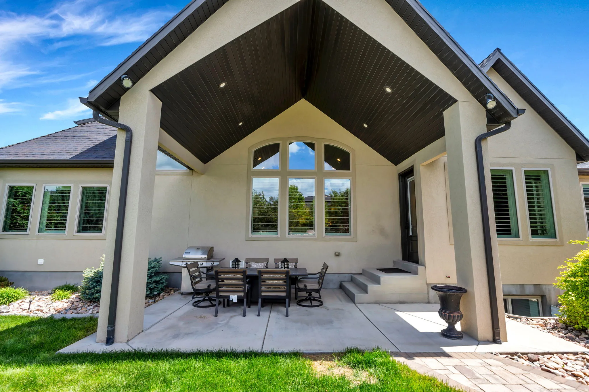 Covered patio with recessed lighting, stucco exterior, vaulted ceiling with wood-finish soffit, arched window detailing, and multi-pane windows with integrated shutters