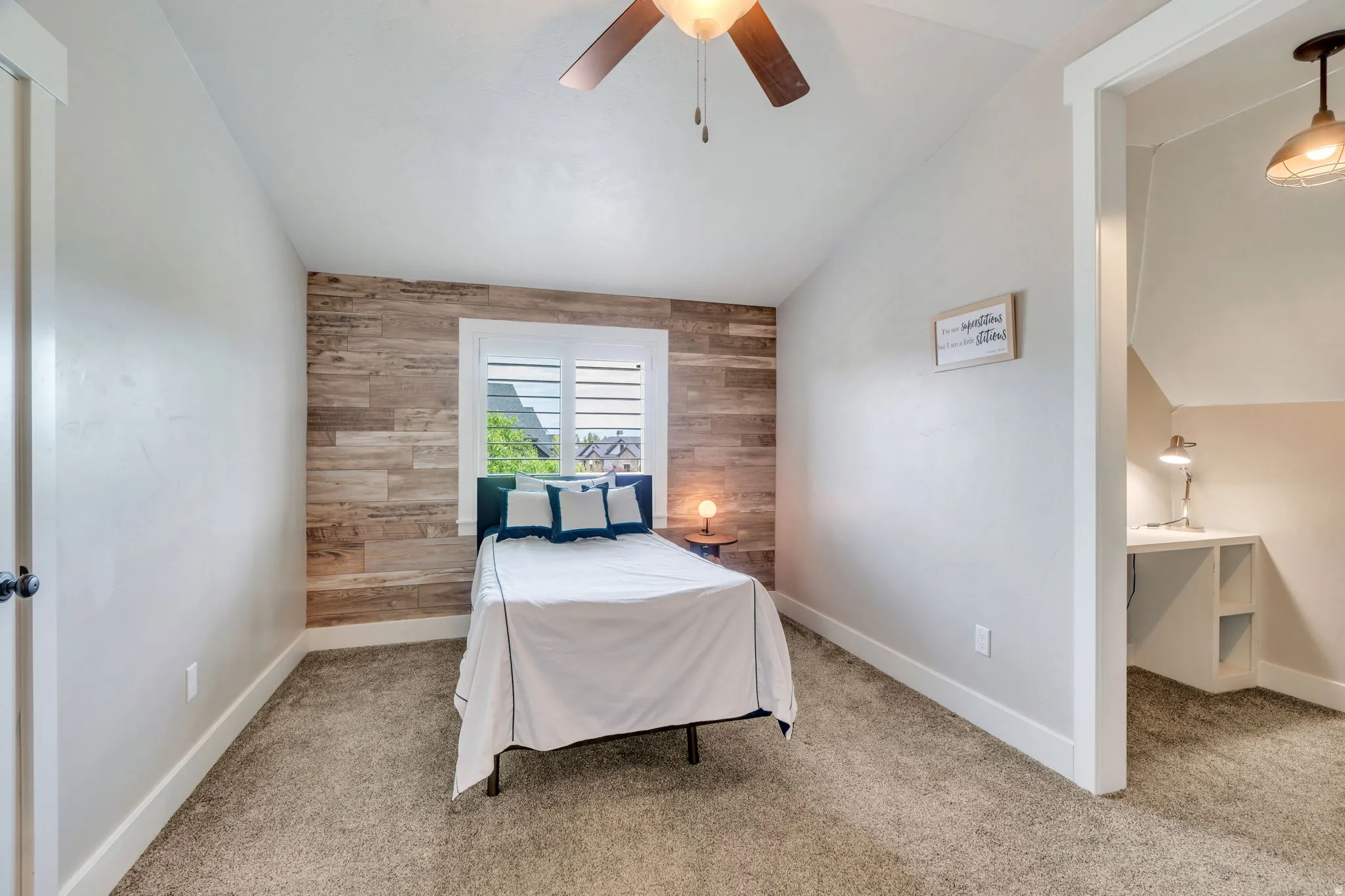 Carpeted room featuring a wood-paneled accent wall, a window with louvered shutters, and a ceiling fan with integrated lighting