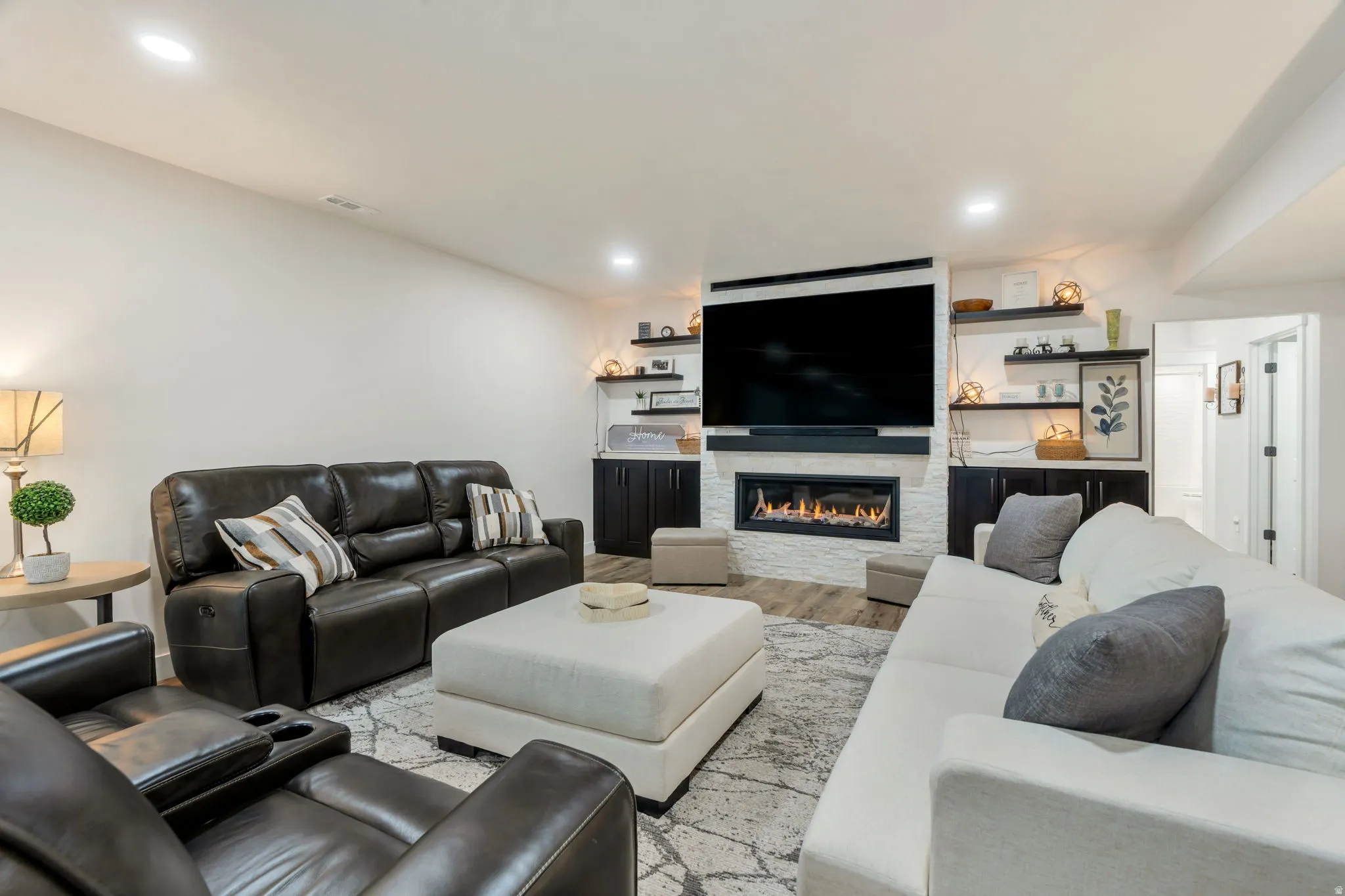 Entertainment area featuring a contemporary linear fireplace with a white stone surround, built-in cabinetry with dark wood-finish doors, floating shelving, recessed lighting, and wood-finish flooring