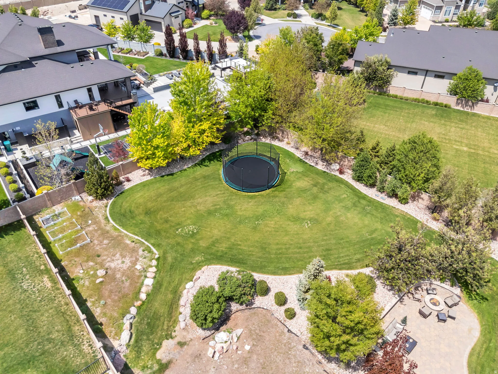 Expansive backyard featuring a manicured lawn, established landscaping, and a paver patio with a built-in fire pit