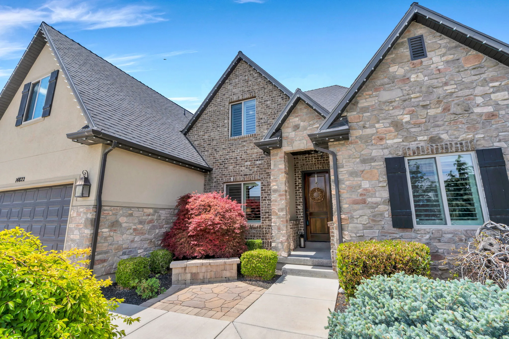 Stone and brick façade residence featuring a gray asphalt shingle roof, dark wood front door, and black window shutters