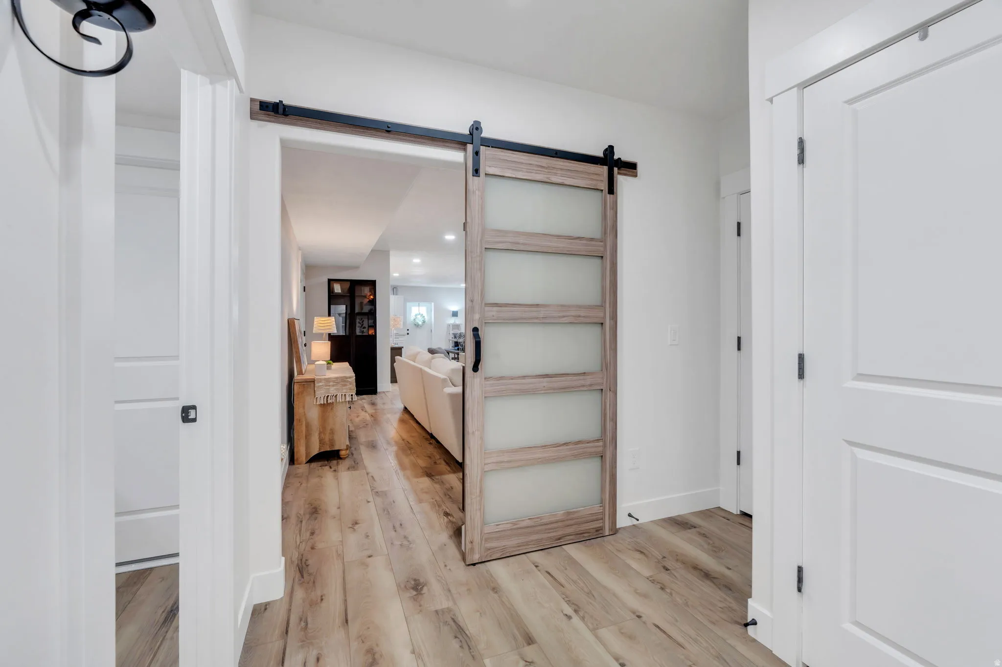 Hallway featuring a barn door with frosted glass panels, wood-finish flooring, and white interior doors with black hardware