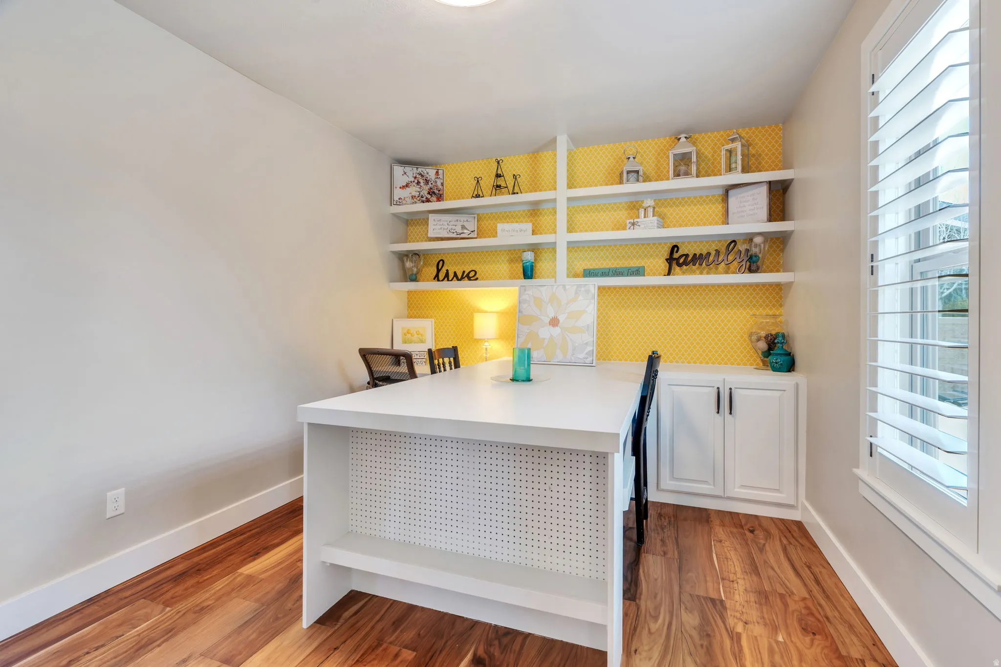 Built-in shelving with integrated base cabinetry, wood-finish flooring, and window with plantation shutters
