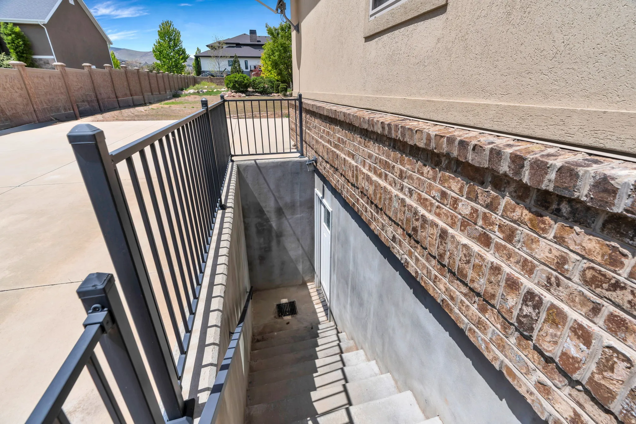 Exterior access featuring concrete stairs, black metal railings, a stucco facade, and a brick accent wall