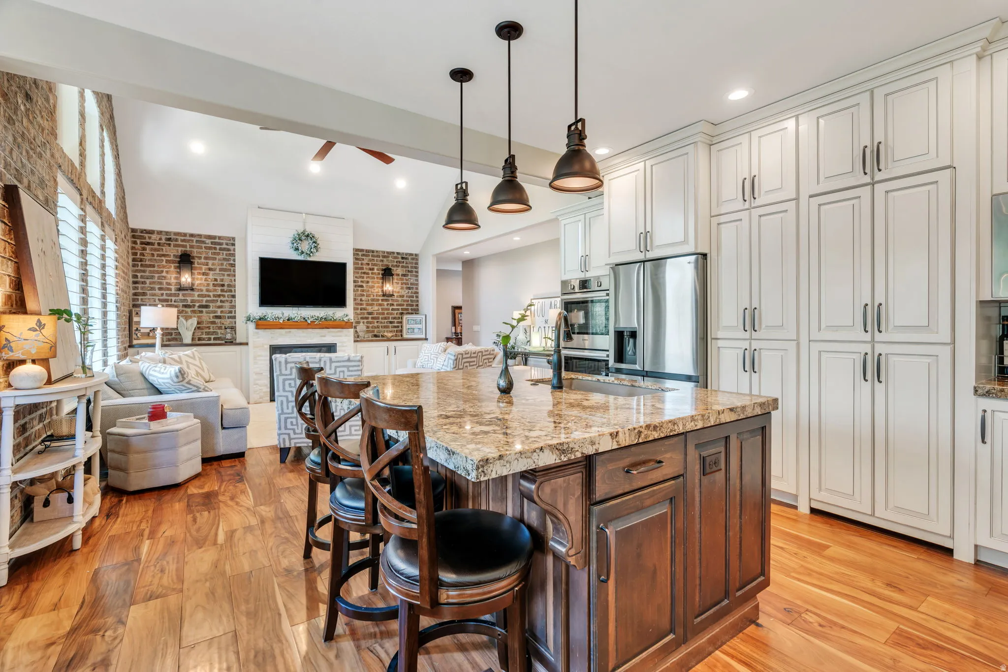 Open-concept kitchen and living area featuring wood-finish flooring, a kitchen island with stone countertop, stainless steel appliances, and extensive white cabinetry