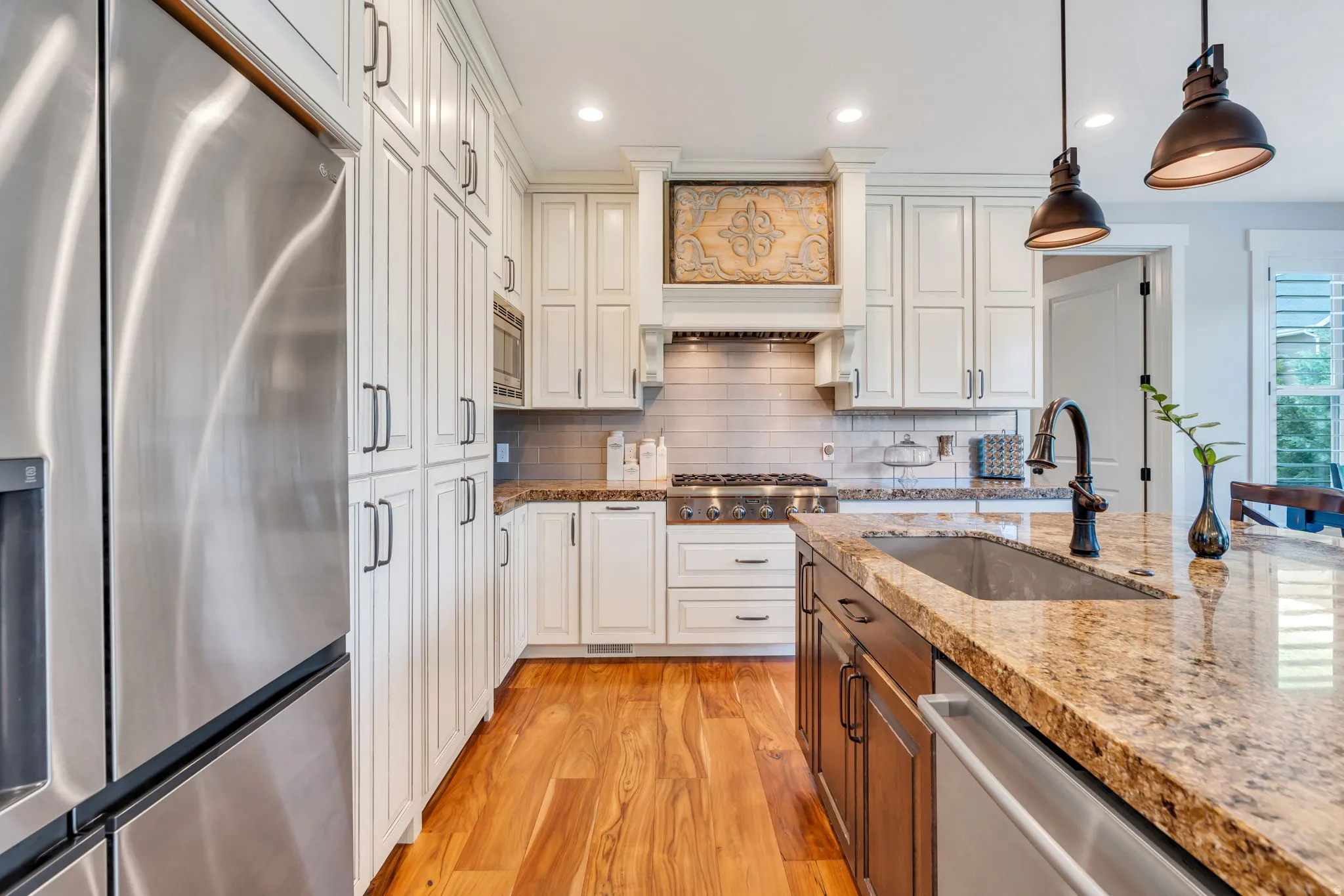Gourmet kitchen with wood-finish flooring, white cabinetry, integrated stainless steel appliances, and a central island with a granite countertop and undermount sink