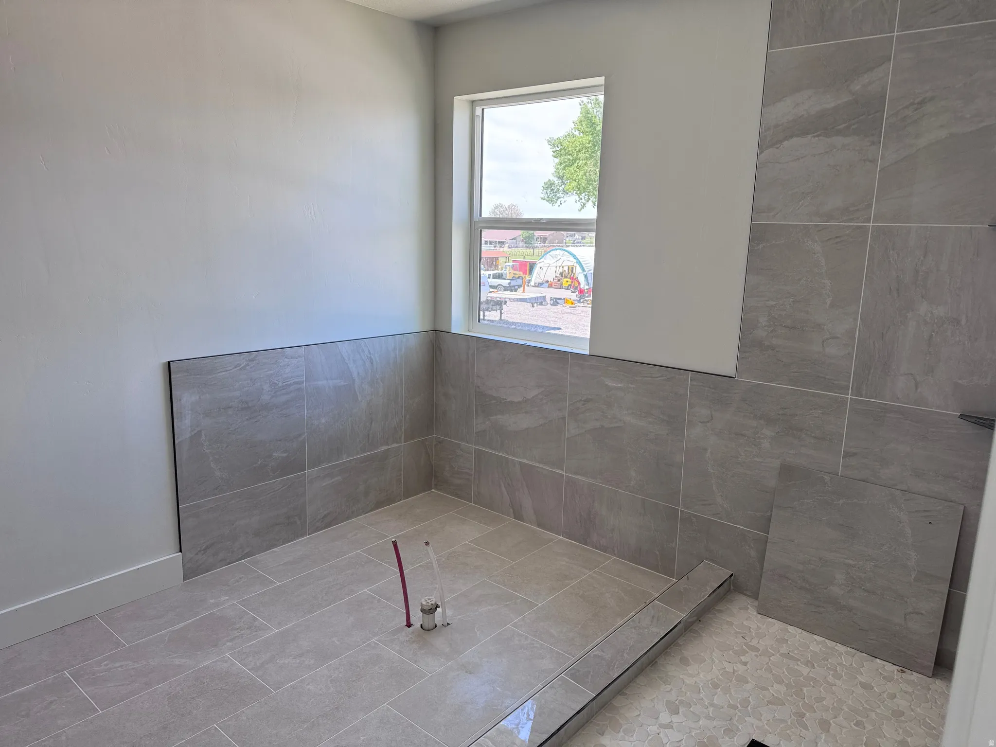 Shower area featuring large format gray tile on walls and floor, a linear drain, and a window with trim