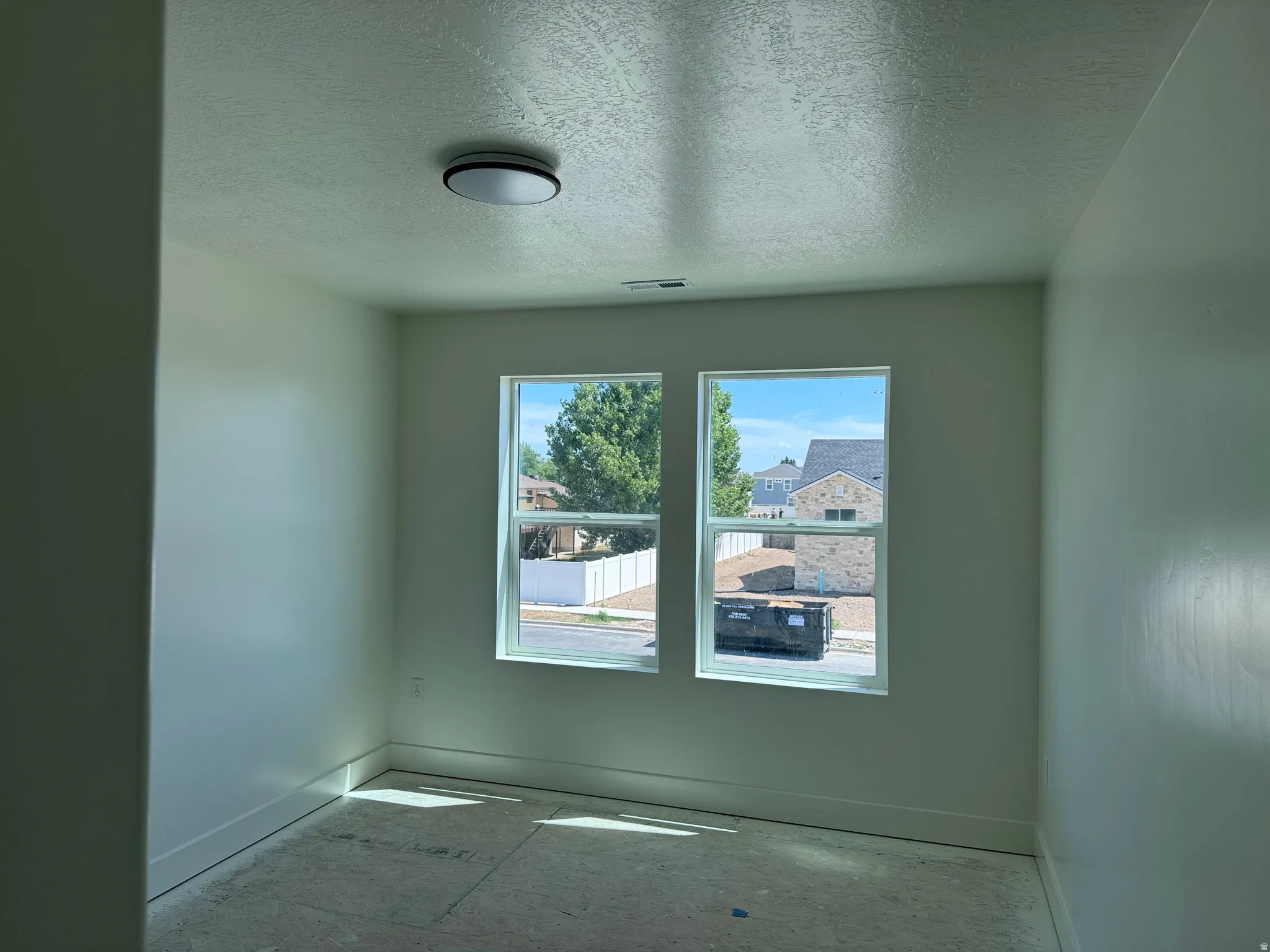Bright room featuring two large windows, a flush-mount ceiling light fixture, and crisp white baseboards
