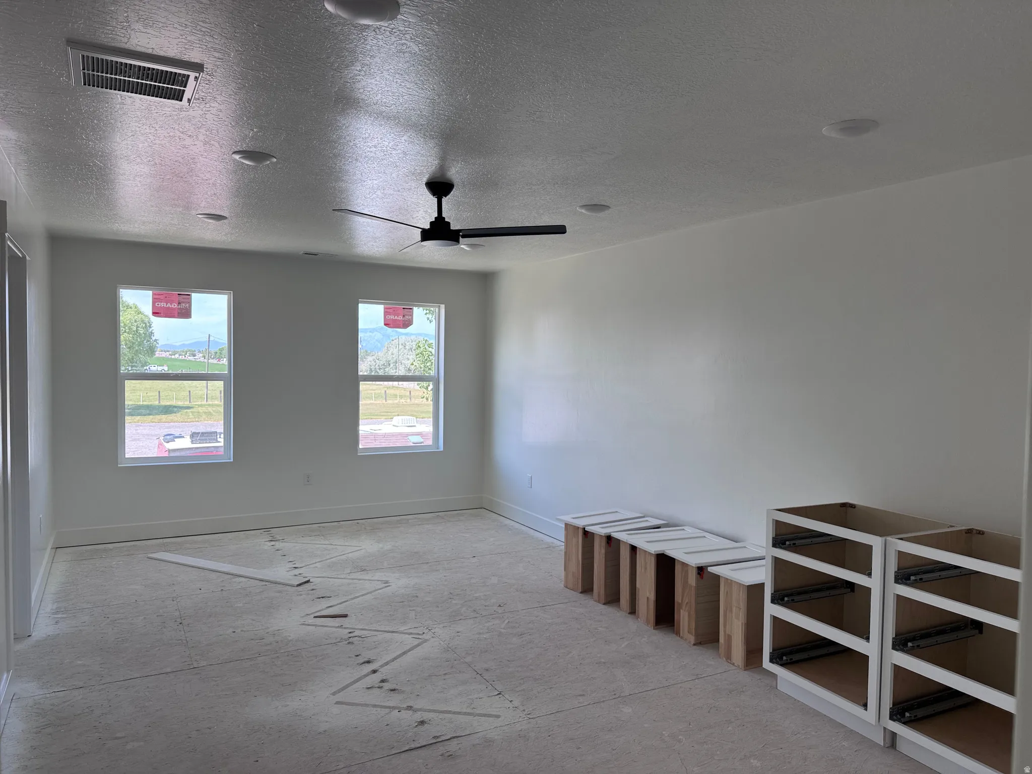 Spacious room with white walls, two large windows, a ceiling fan, and recessed lighting