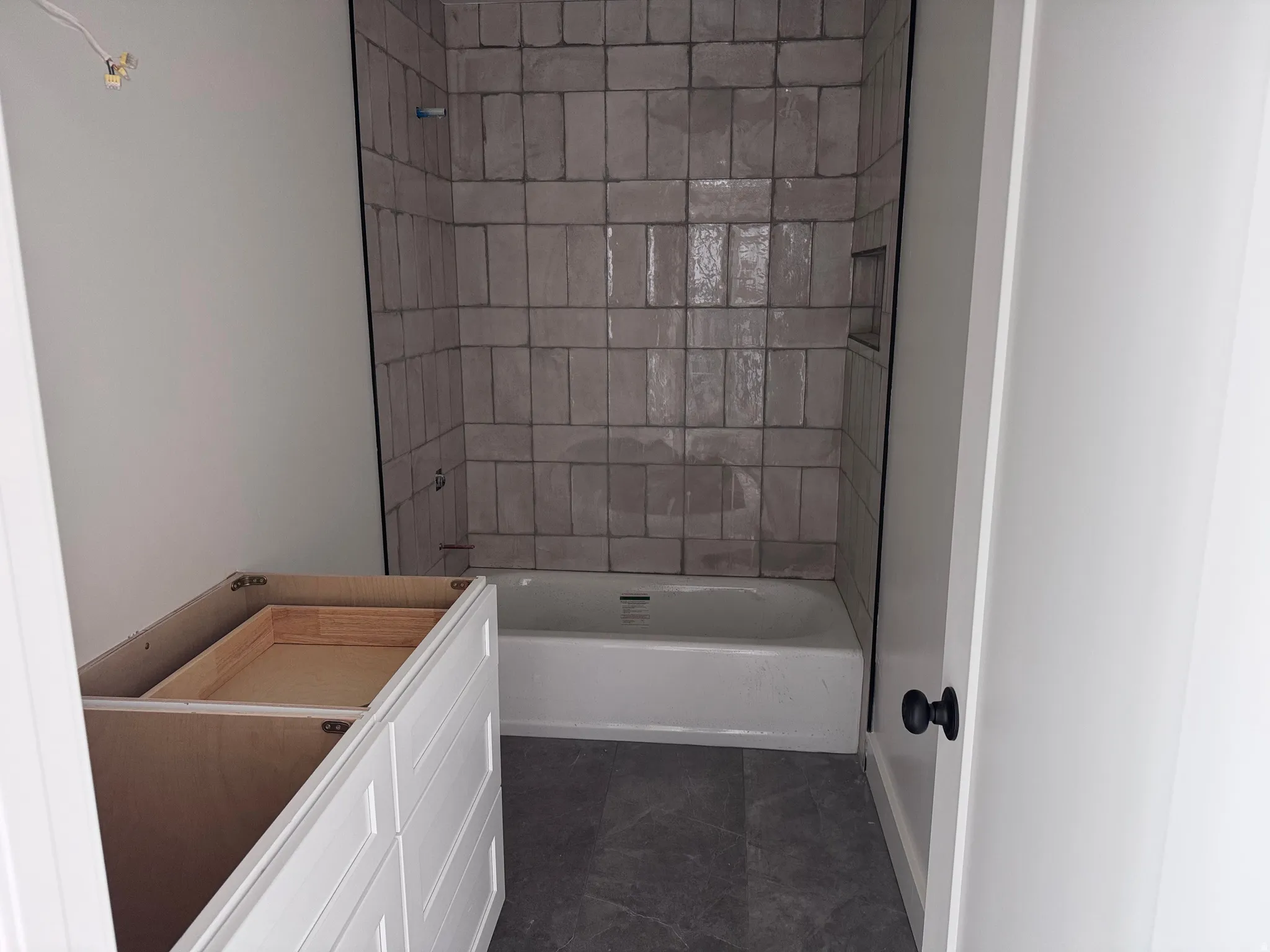 Newly tiled tub surround with an integrated shower niche, a white soaking tub, and dark floor tiling