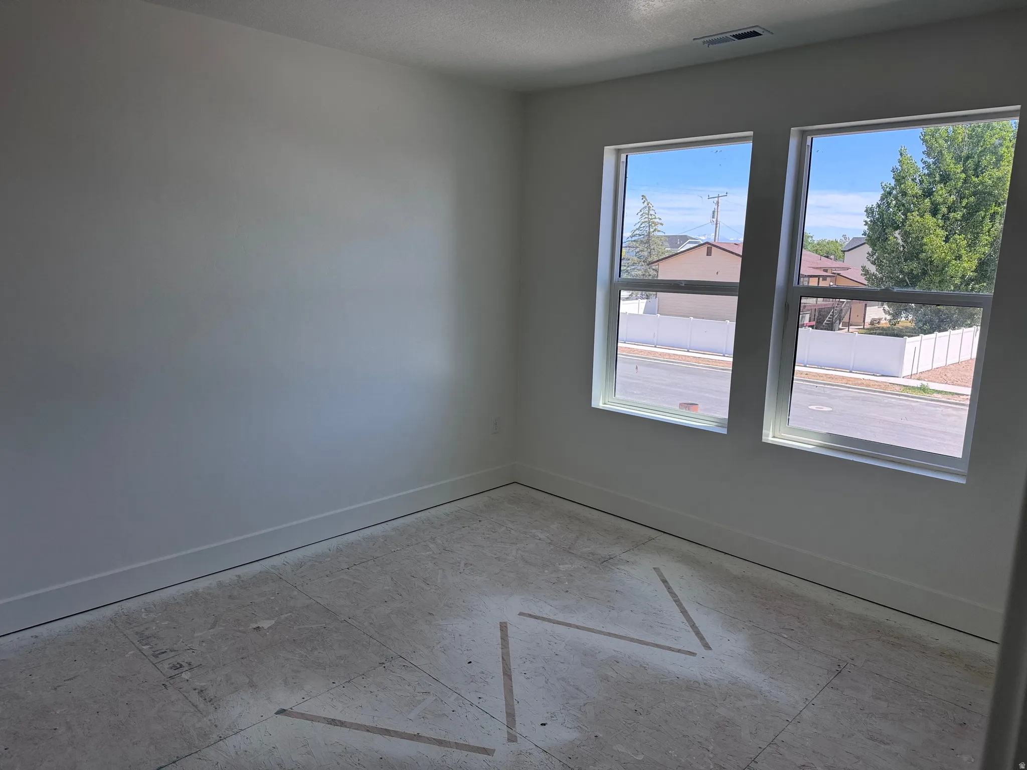 Bright interior space featuring two large windows, white walls, and a subfloor ready for finish