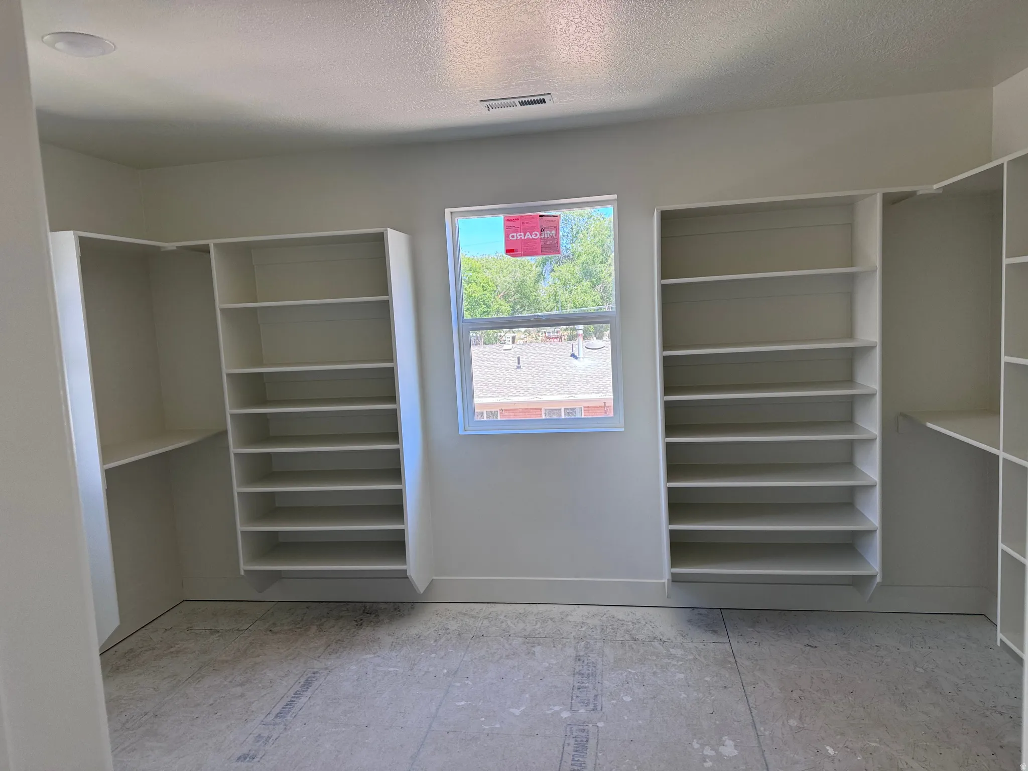 Spacious room featuring multiple built-in shelving units, a recessed ceiling light, a window providing natural light, and a vent