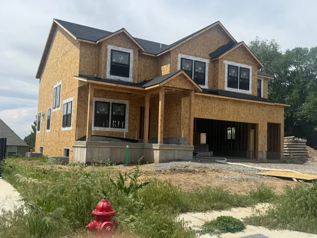 Newly constructed home featuring a prominent two-story design with a covered front porch, dark-framed windows, and a two-car garage opening