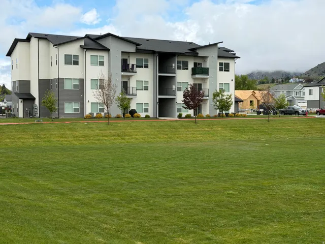 Modern multi-story residential building featuring a neutral color palette, dark roofing, and multiple balconies