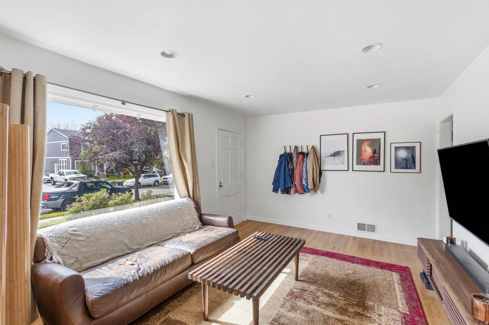 Living area featuring a large picture window, light wood-finish flooring, recessed lighting, and a white paneled entry door