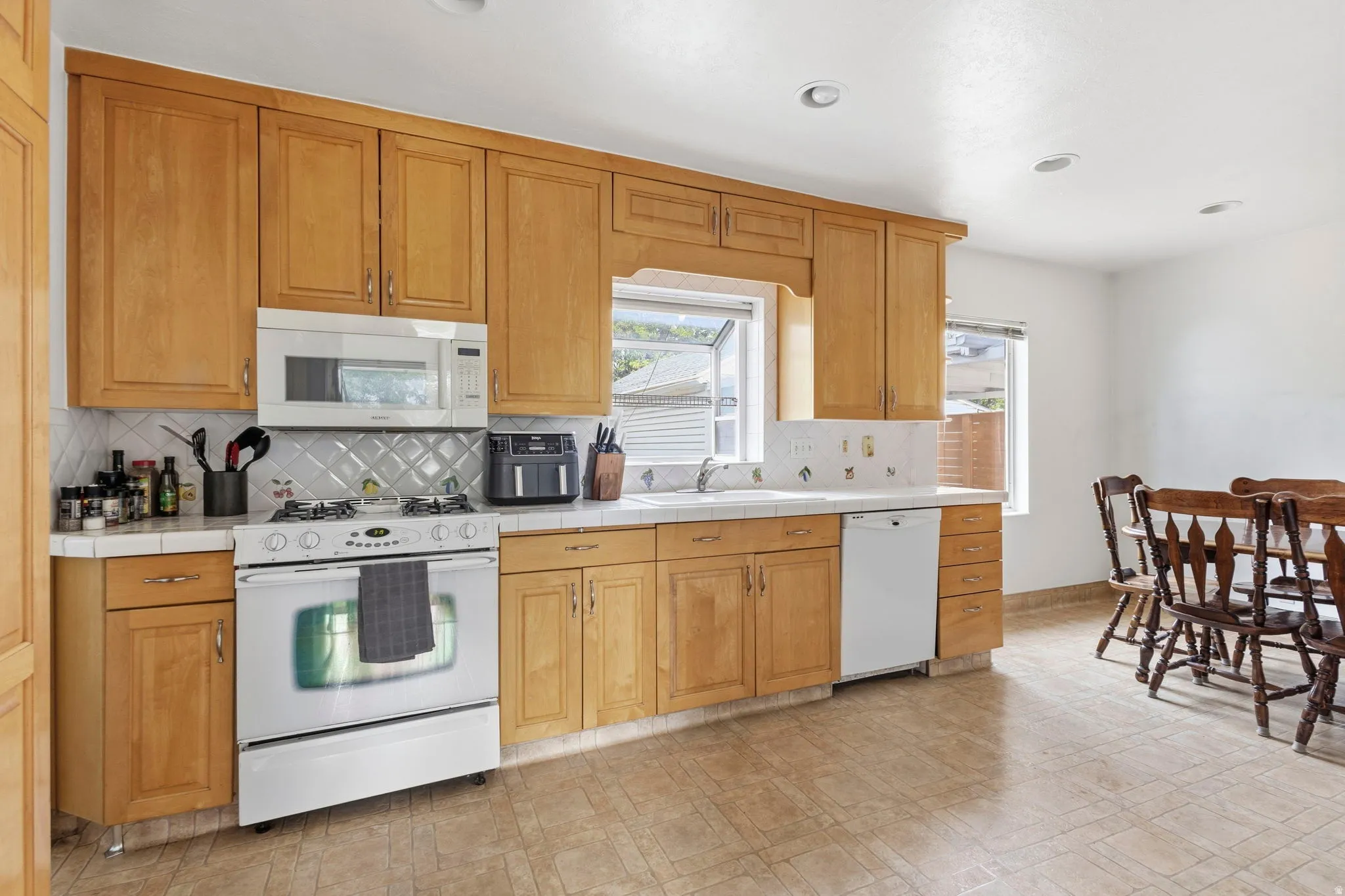 Kitchen featuring wood cabinetry, white tile countertops, and a white appliance suite including a range, microwave, and dishwasher