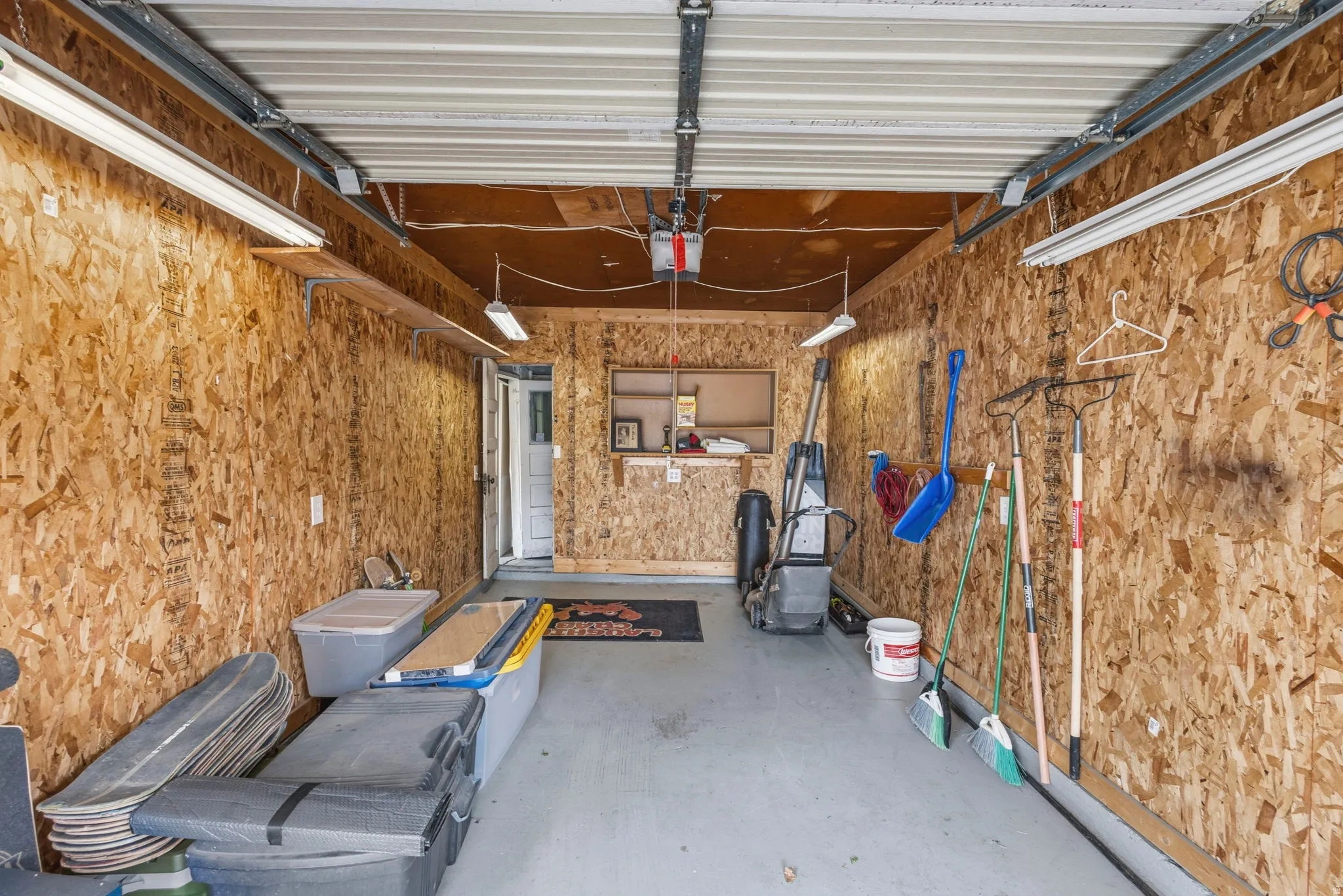Garage space featuring wood-finish wall panels, overhead fluorescent lighting, and a painted concrete floor