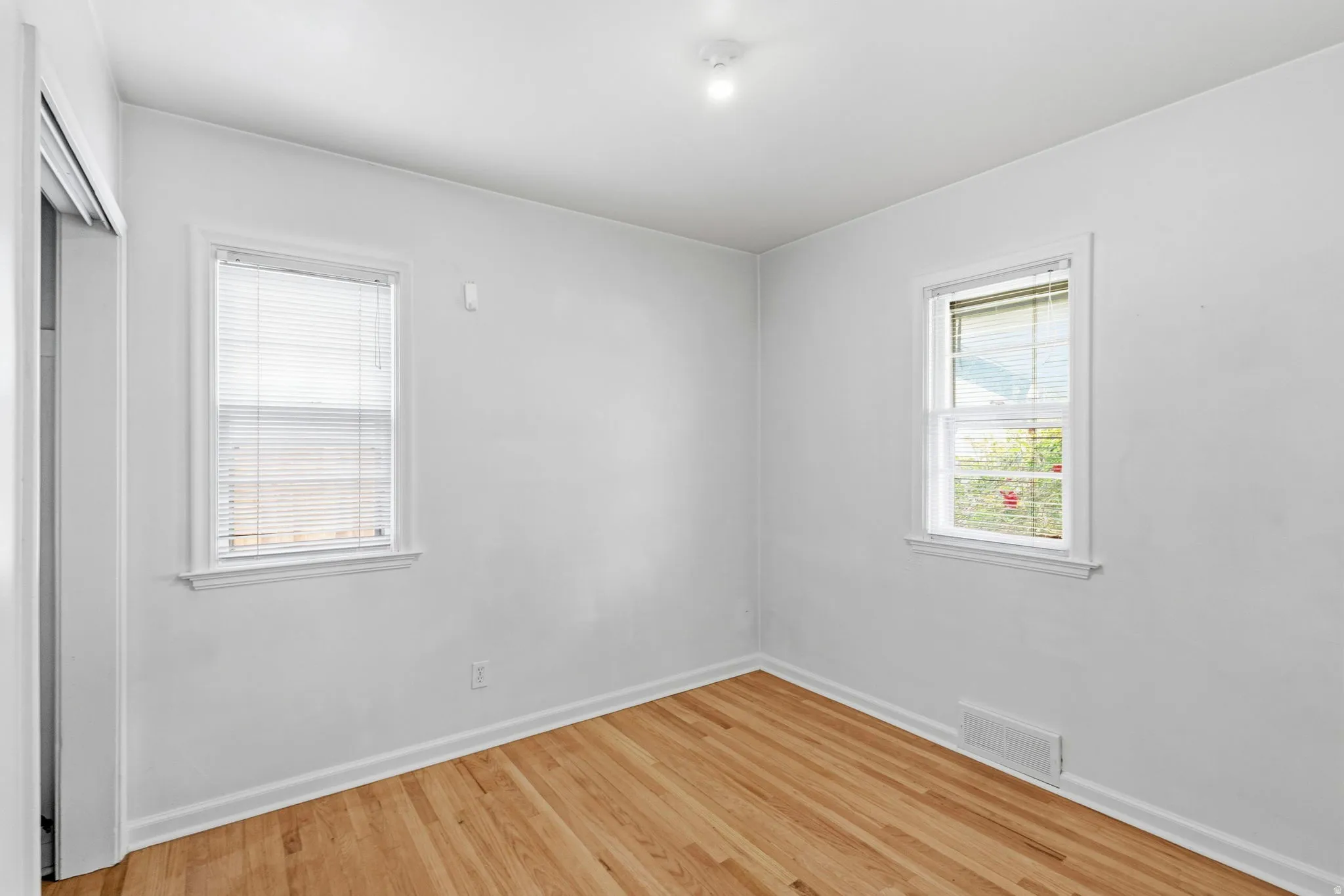 Room with wood-finish flooring, white baseboards, and two windows with white trim